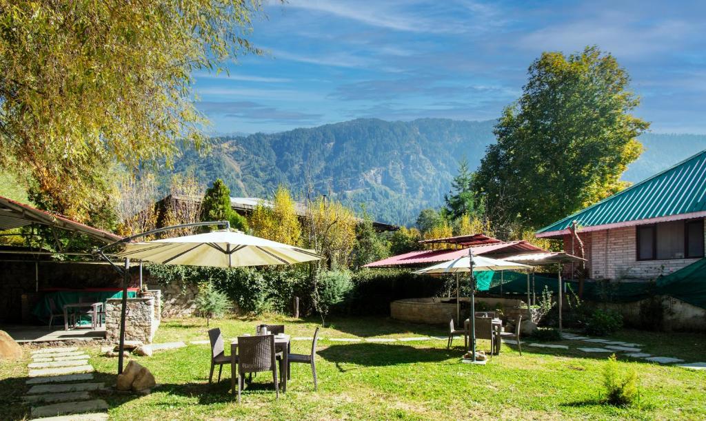 a yard with chairs and umbrellas in the grass at Treebo Trend Ambika Residency Near Hidimba Devi Temple in Manāli