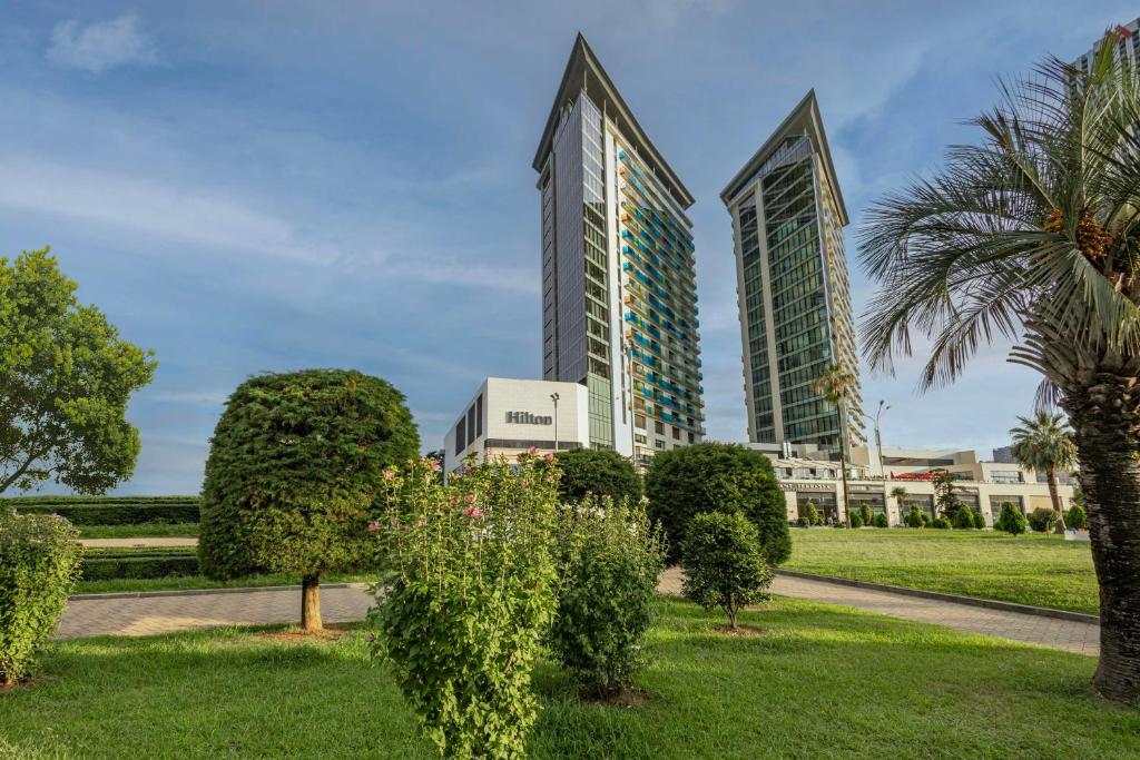 park przed dwoma wysokimi budynkami w obiekcie Hilton Batumi w mieście Batumi