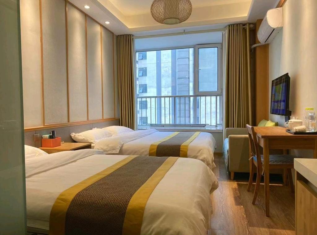 青島市にあるQingdao Shuiyunjian Apartmentのベッド2台、デスク、窓が備わるホテルルームです。