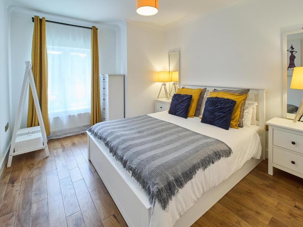 a white bedroom with a large bed with blue and yellow pillows at Host & Stay - Bellflower Mews in Canterbury