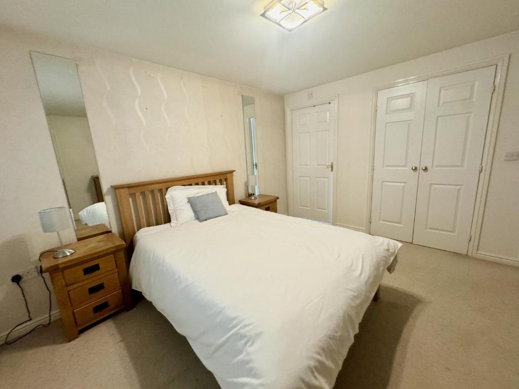 a bedroom with a large white bed and a night stand at Elvetham Nest Guesthouse, Basingstoke in Basingstoke