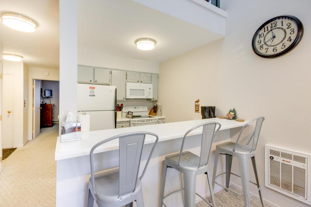 a kitchen with white counter chairs and a clock on the wall at Cozy Condo with Balcony - Near Big Sky Resort! in Big Sky