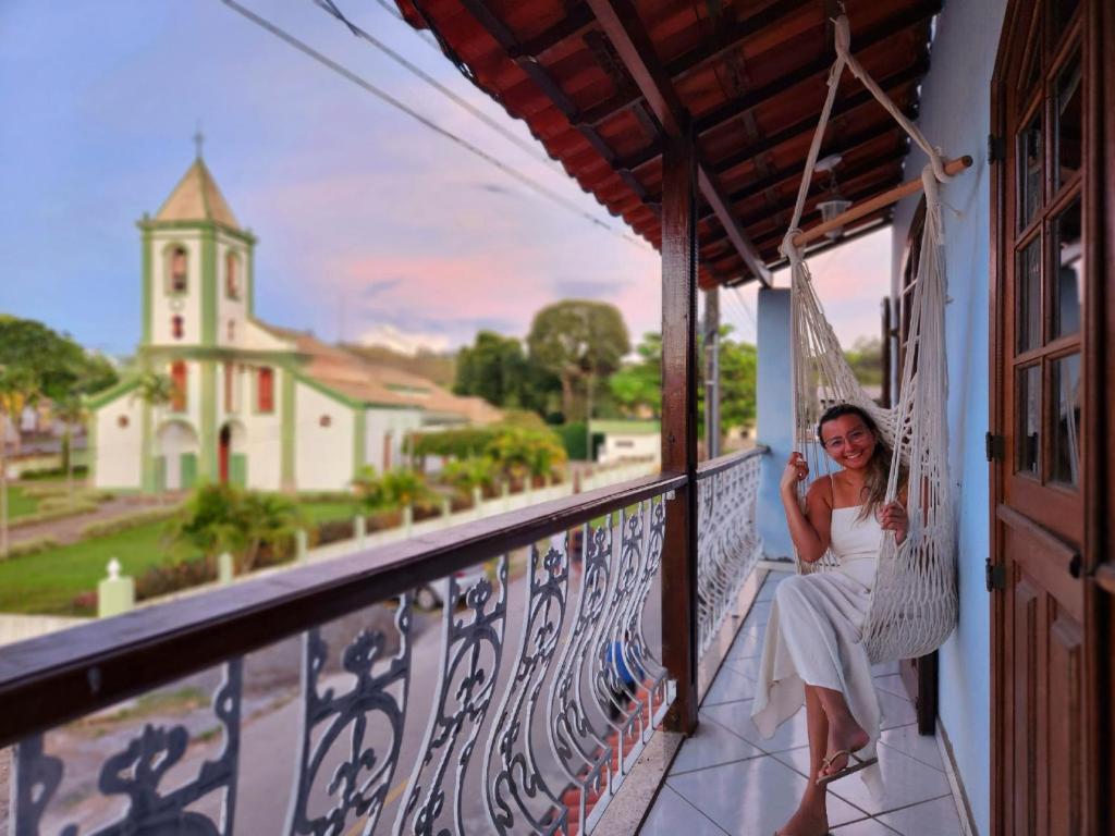 une femme assise dans un hamac sur un balcon avec une église dans l'établissement PousaDinháChica Hospedagem perto de Tiradentes Minas, à São João del Rei