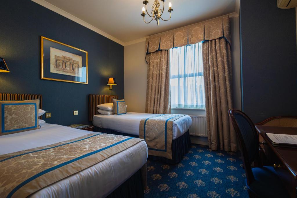 a hotel room with two beds and a desk and a window at London Lodge Hotel in London