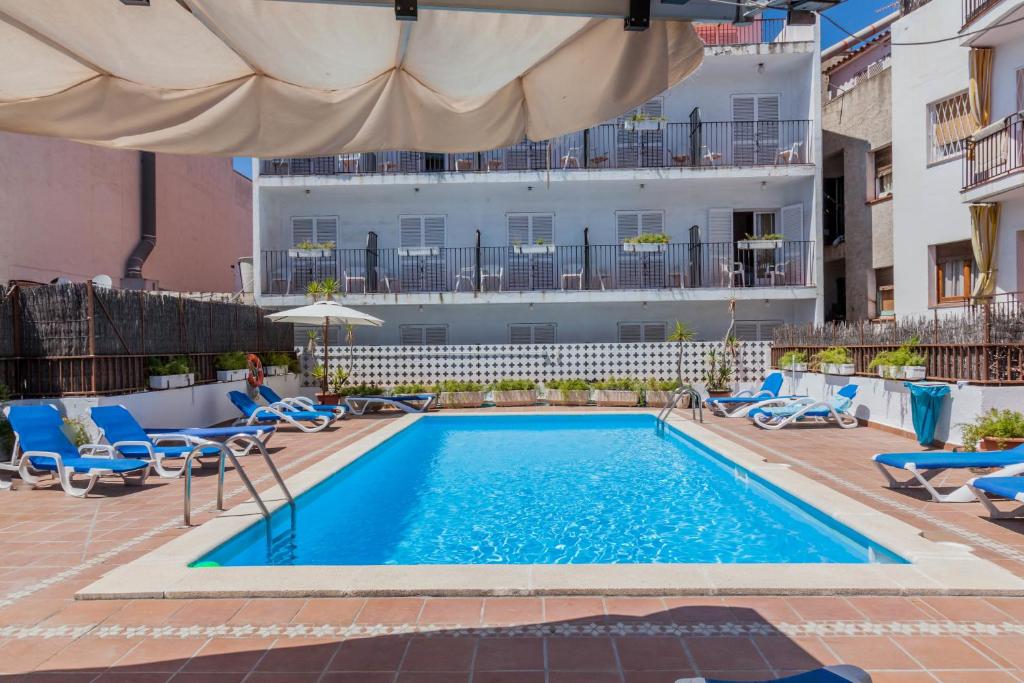 a swimming pool with chairs and a building in the background at El Cid in Sitges