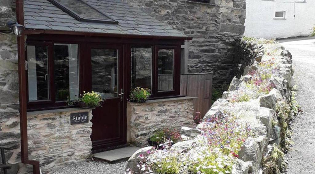 a stone house with a door and some flowers at The Stable, Broughton Beck, near Ulverston in Spark Bridge