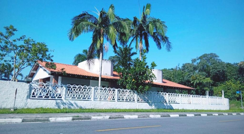 a house with a white fence and palm trees at Lemon Suítes e Pousada - Indaiá Riviera in Bertioga