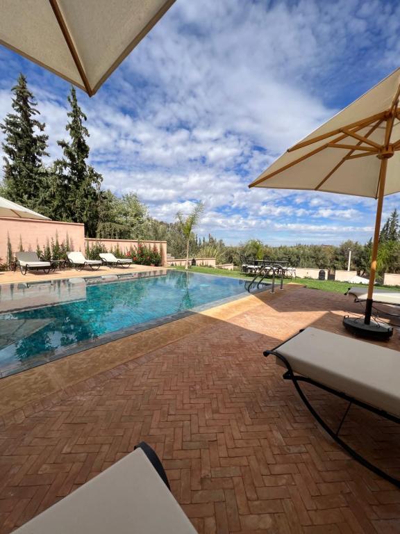 a swimming pool with a table and an umbrella at Riad Timskrine in Marrakech