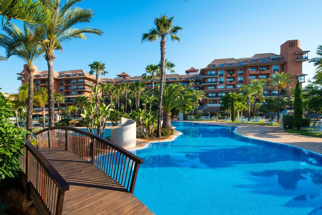 un complexe avec une piscine bordée de palmiers et un hôtel dans l'établissement Puerto Antilla Grand Hotel, à Islantilla