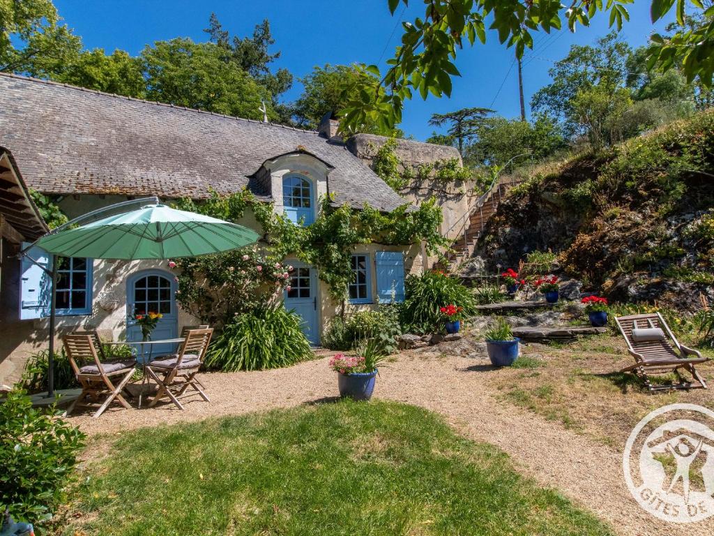 un cottage con sedie e un ombrellone di fronte di Charmante maison avec jardin clos près de la rivière Louet - FR-1-622-37 a Denée