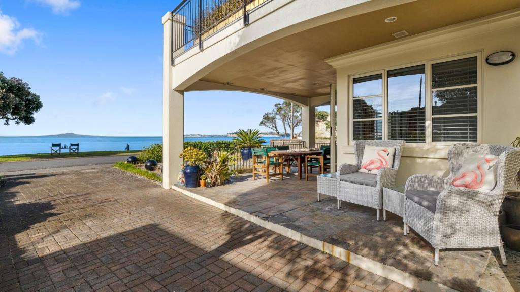 um alpendre com 2 cadeiras e uma mesa com vista para o oceano em Beachfront Beauty em Whangaparaoa