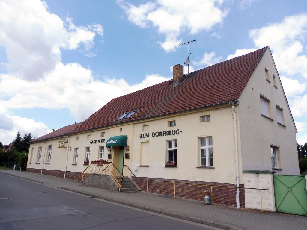 um edifício branco com um telhado castanho numa rua em Ferienwohnung "Zum Dorfkrug" em Kerkwitz