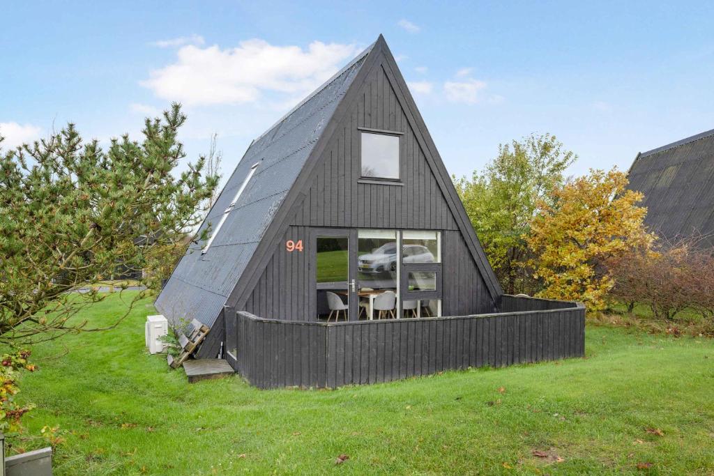 a black triangular house on a grassy field at Summer House At Himmerland Golf Resort in Farsø