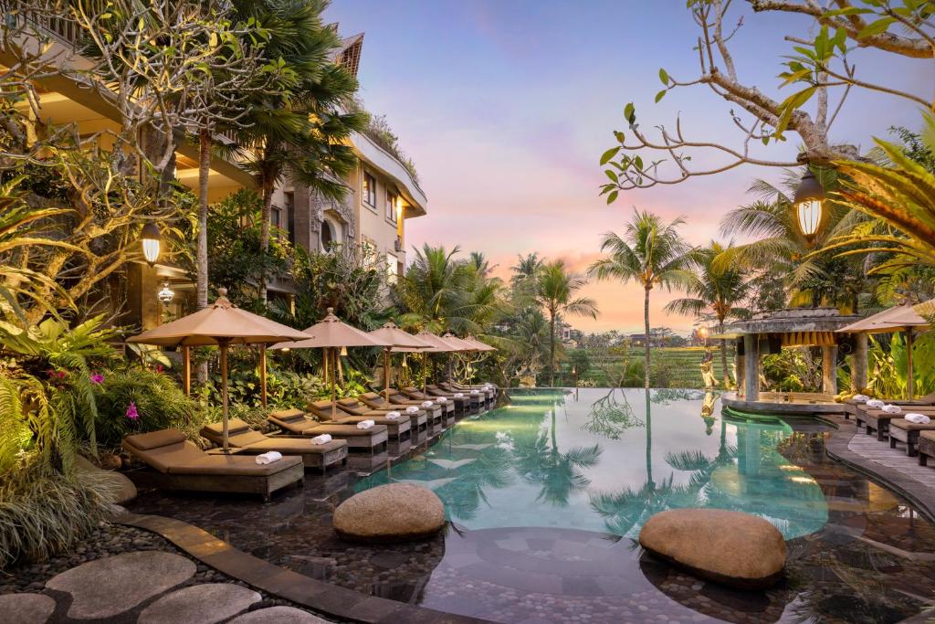 a pool at a resort with chairs and umbrellas at Kuwarasan A Pramana Experience in Ubud