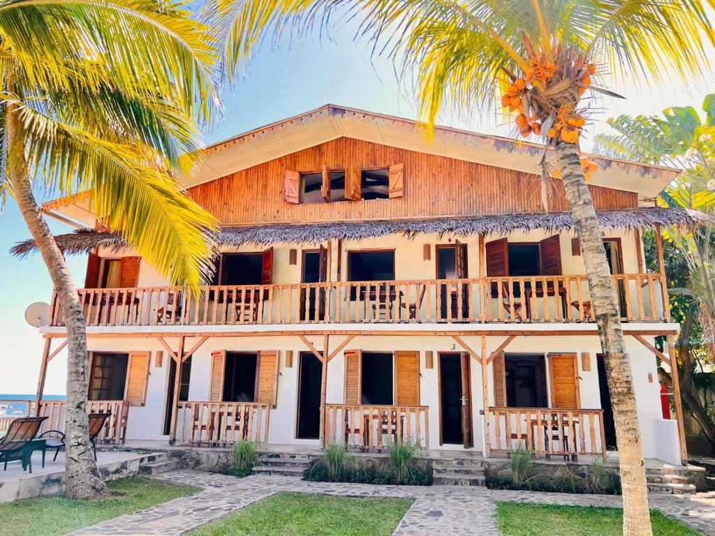 ein Haus mit einem Balkon und zwei Palmen in der Unterkunft L'Ylang Ylang Auberge d'AMBATOLOAKA in Ambatoloaka