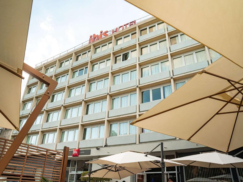 un bâtiment d'hôtel avec des parasols en face de celui-ci dans l'établissement Ibis Alès Centre Ville, à Alès