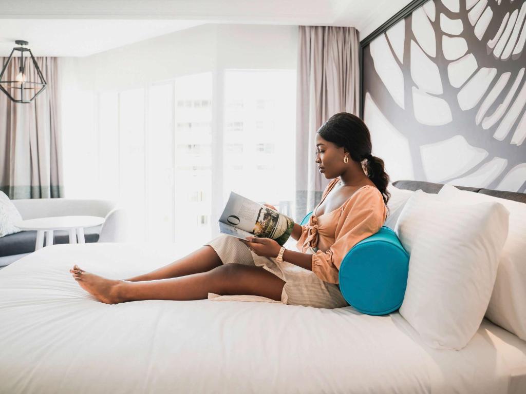 a woman sitting on a bed reading a book at Pullman Cairns International in Cairns