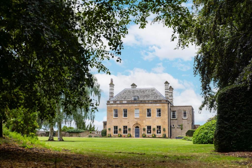 une vieille maison sur un champ vert avec des arbres dans l'établissement Cuckney House - Georgian Manor on a country estate - Sleeps 31, à Cuckney