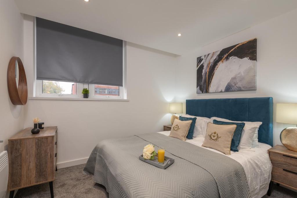 a bedroom with a bed with a blue headboard and a window at Thornhill House Serviced Apartments in Wakefield
