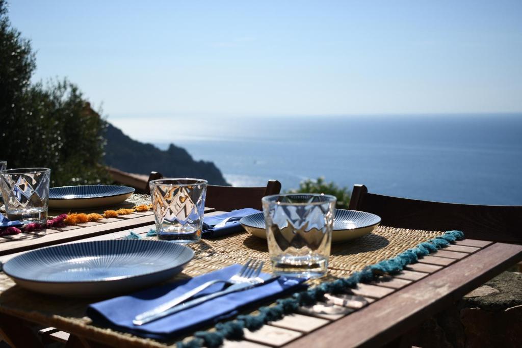 a table with plates and glasses on a table with the ocean at BB24 - Cottage il Puntino in Porto Santo Stefano