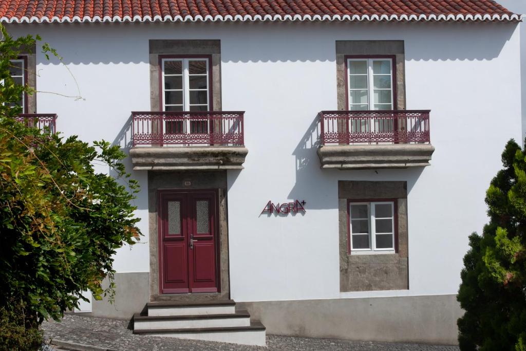 a white house with red doors and balconies at AngrA + in Angra do Heroísmo