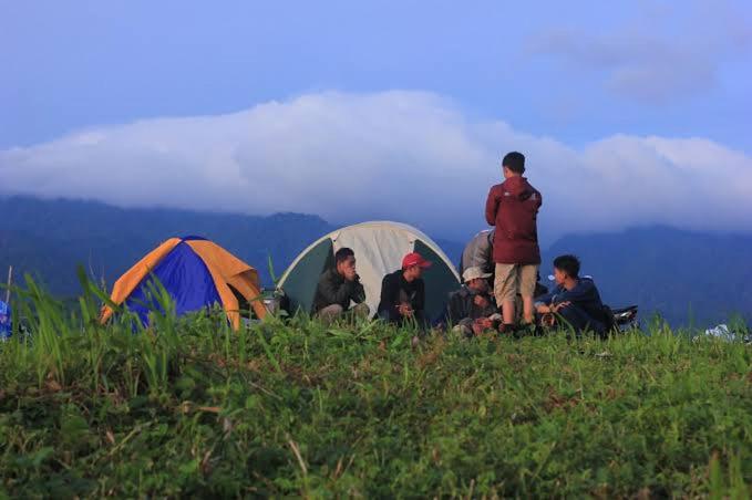a group of people sitting on a hill with tents at view cemping glamping in Bukittinggi