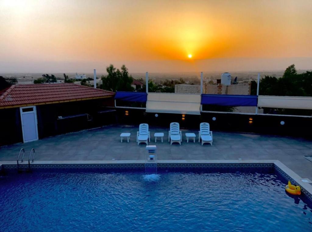 a swimming pool with chairs and a sunset in the background at Cali Chalet in Al Karāmah