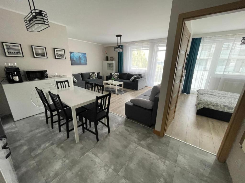 sala de estar y comedor con mesa y sillas en Bliżej Morza Deluxe Apartmenty, en Kołobrzeg