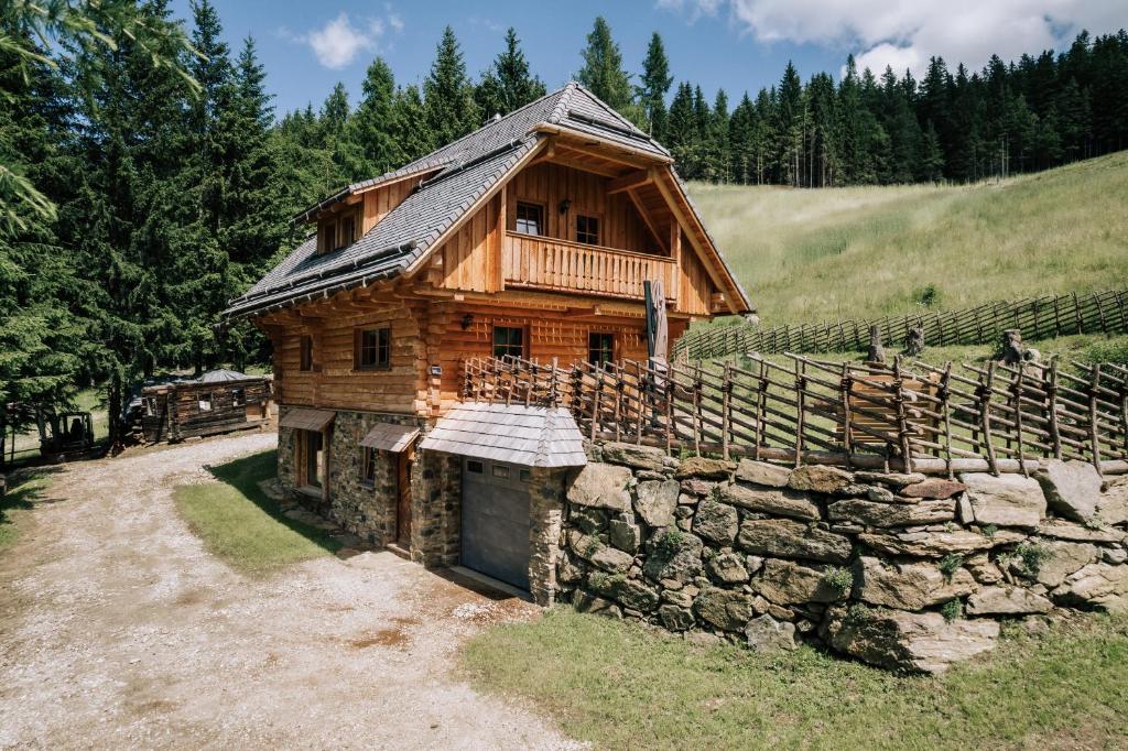 Cabaña de madera con pared de piedra y valla en Webertonihütte en Bad Sankt Leonhard im Lavanttal