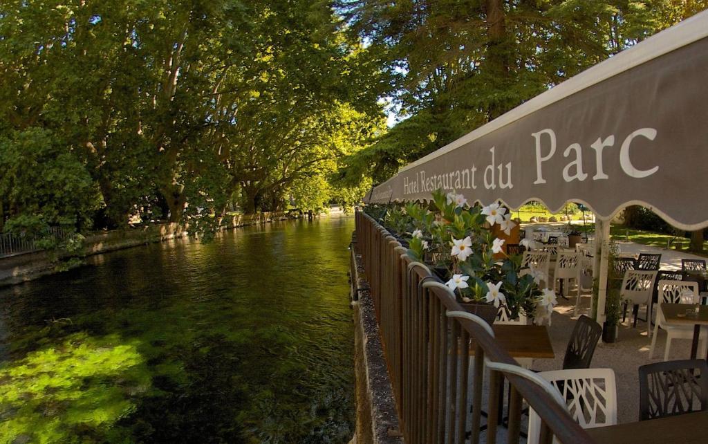 une rivière avec des tables et des chaises à côté d'un bâtiment dans l'établissement Hotel Restaurant du Parc en Bord de Rivière, à Fontaine-de-Vaucluse