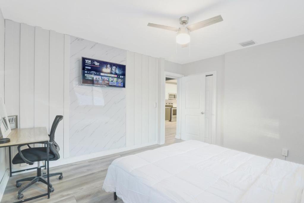 een witte slaapkamer met een bed, een bureau en een televisie bij Spacious and luxurious home centrally located between Miami and Ft. Lauderdale in Miramar