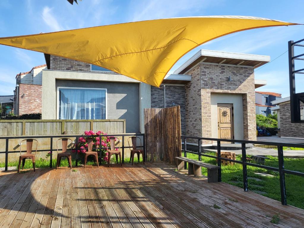 a yellow umbrella over a deck with a table and chairs at House MOZAC in Jeju