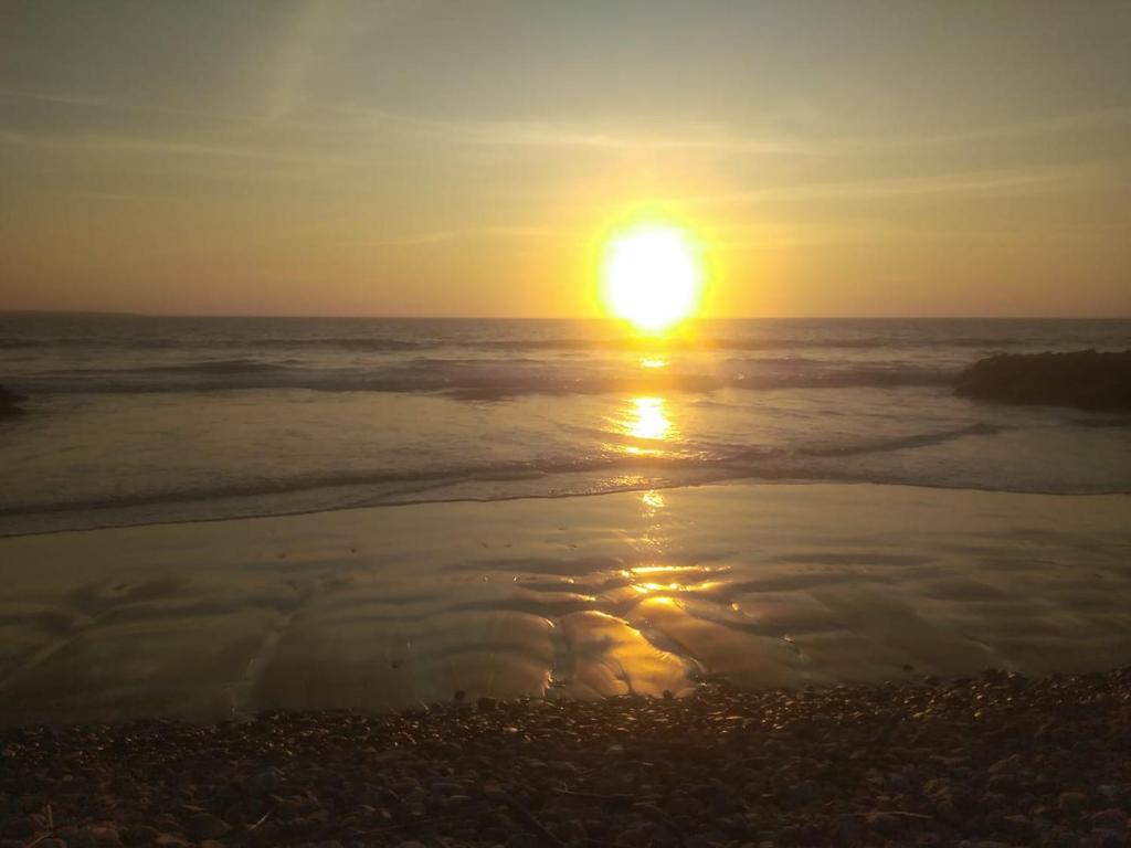 una puesta de sol en la playa con el sol reflejándose en el agua en MERINO HOUSE COLAN BEACH, en Paita