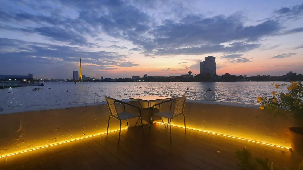 a table and two chairs sitting on a deck near the water at Riverfront house/Chao phraya river/Baan Rimphraya in Bangkok