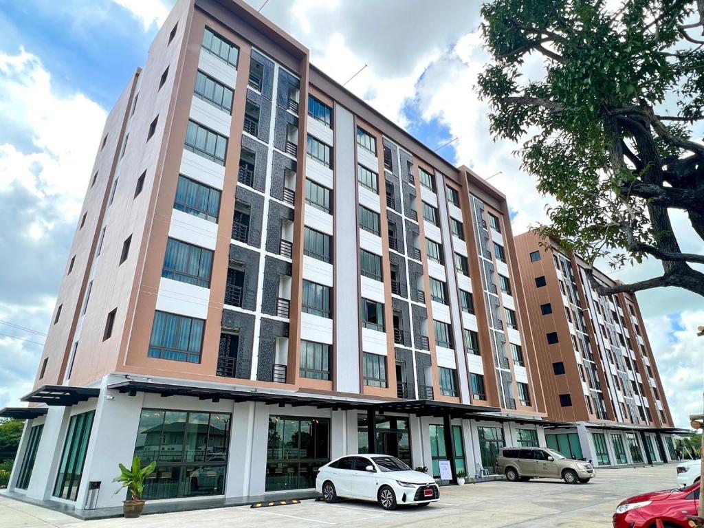 Un gran edificio con coches aparcados delante. en JIA HAUS Hotel Apartment, en Buriram