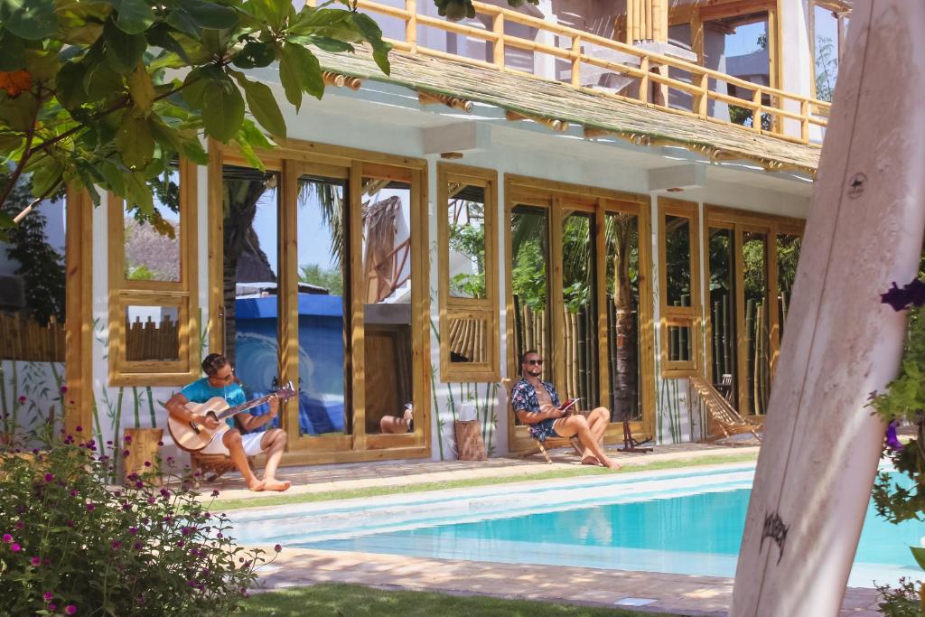 two men sitting next to a house with a pool at SHANTI SURF CAMP in El Paredón Buena Vista