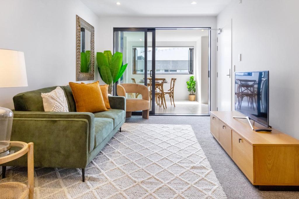 ein Wohnzimmer mit einem grünen Sofa und einem TV in der Unterkunft Heart of Christchurch CBD Hideaway 2bed 1 bath in Christchurch