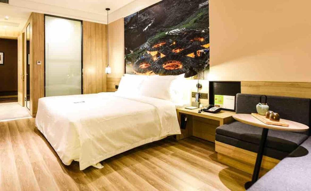 a bedroom with a bed and a table and a painting at Atour Hotel Xiamen Haicang Gulangyu Pier Seaview in Xiamen