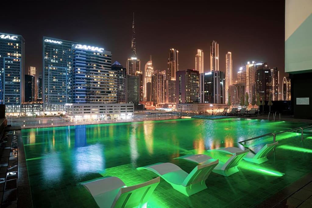 een zwembad met stoelen en 's nachts een skyline van de stad bij Waves Holiday Homes - 15 Northside, Tower 1, Two Bedroom in Dubai