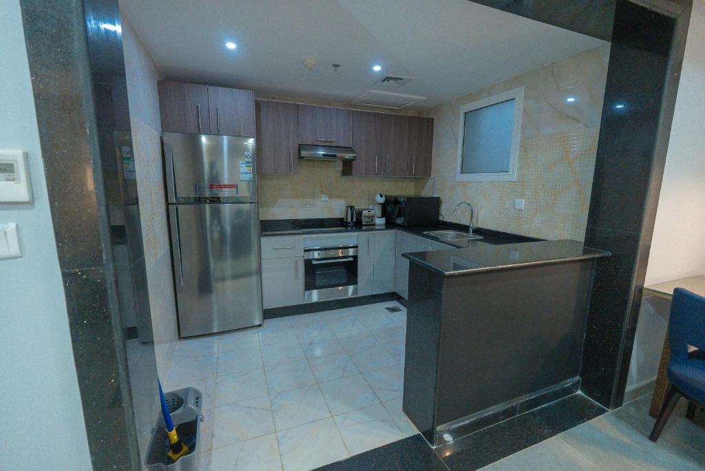 una cocina con nevera de acero inoxidable y armarios en La Cordia Hotel Apartment لاكورديا للشقق الفندقية en Adh Dhahirah