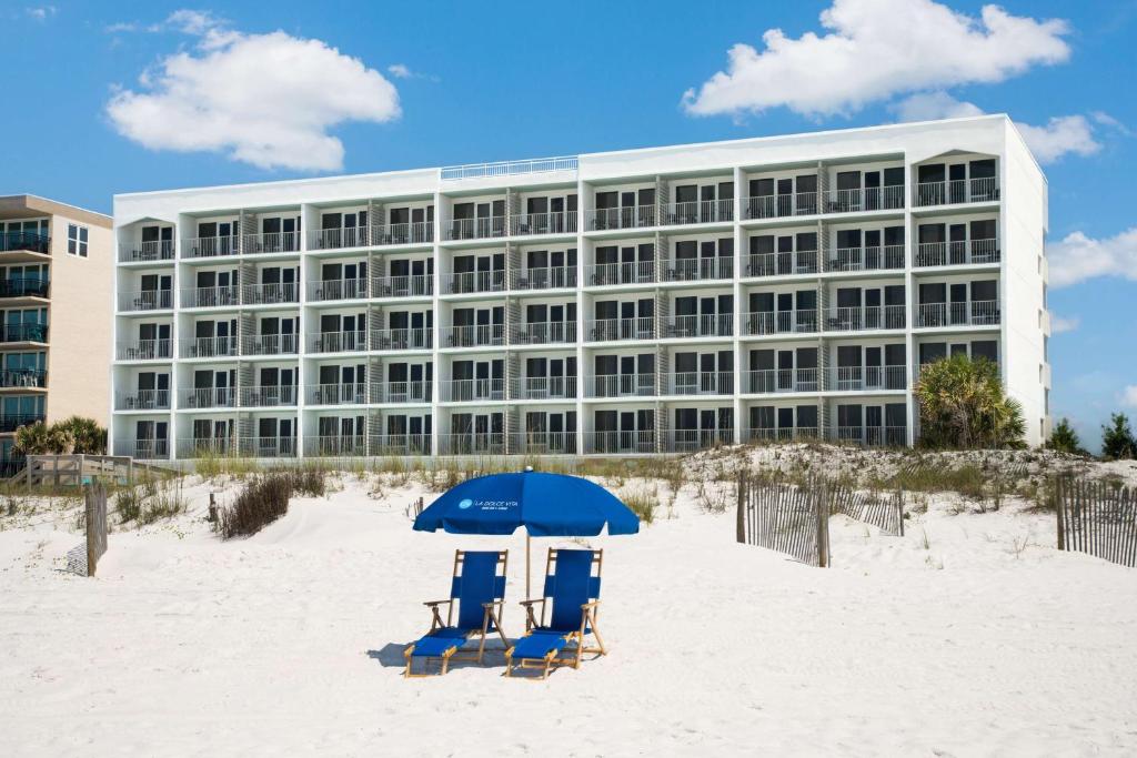 twee stoelen en een parasol op het strand voor een gebouw bij Beal House Fort Walton Beach, Tapestry Collection By Hilton in Fort Walton Beach