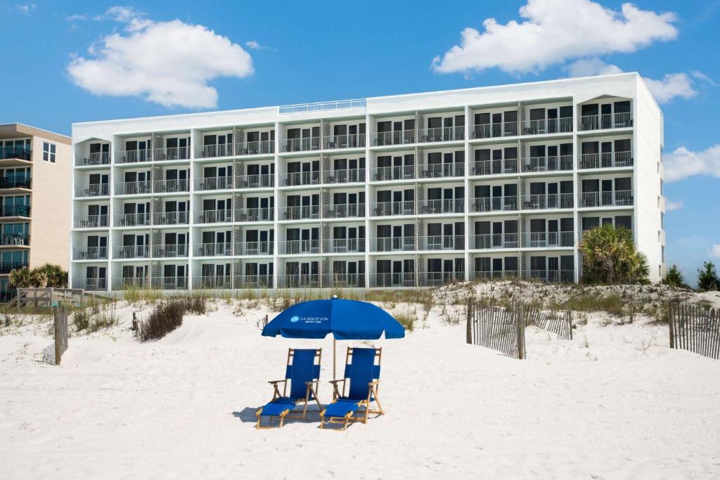two chairs and an umbrella on the beach in front of a building at Beal House Fort Walton Beach, Tapestry Collection By Hilton in Fort Walton Beach
