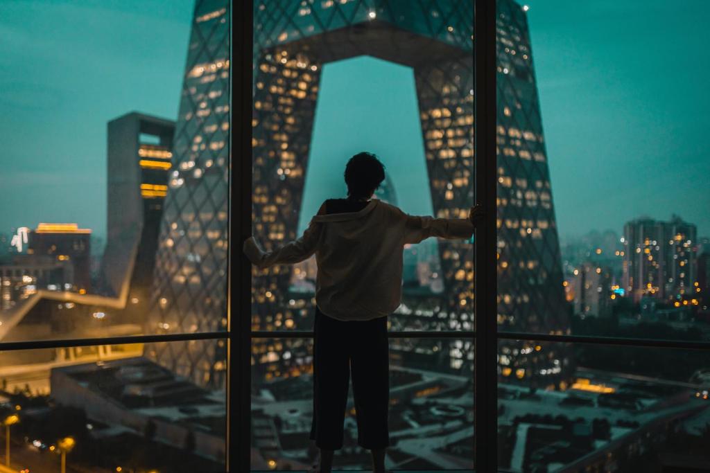 Un homme debout dans une fenêtre donnant sur une ville dans l'établissement JEN Beijing by Shangri-La, à Pékin