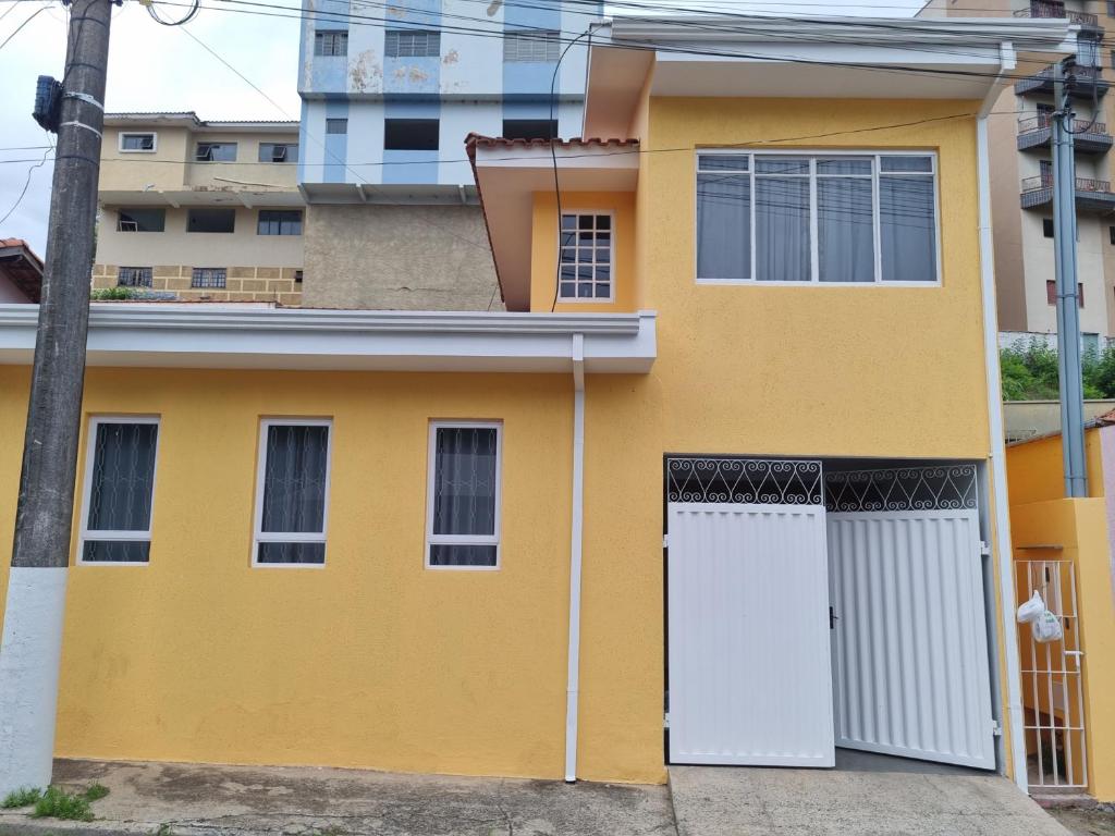 a yellow house with a white door at Casa com dois quartos,dois banheiros,sendo uma suíte,sala de estar cozinha e garagem in Poços de Caldas