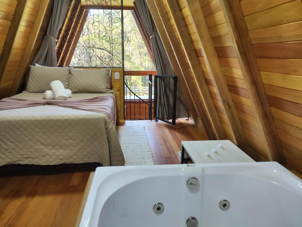 uma casa de banho com uma banheira, uma cama e uma janela em Chalé Magia das Hortênsias em Canela