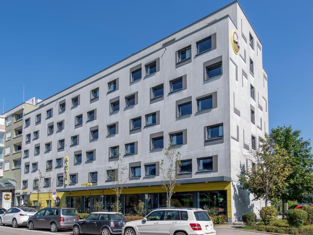 un edificio blanco con coches estacionados frente a él en B&B Hotel München City-West, en Múnich