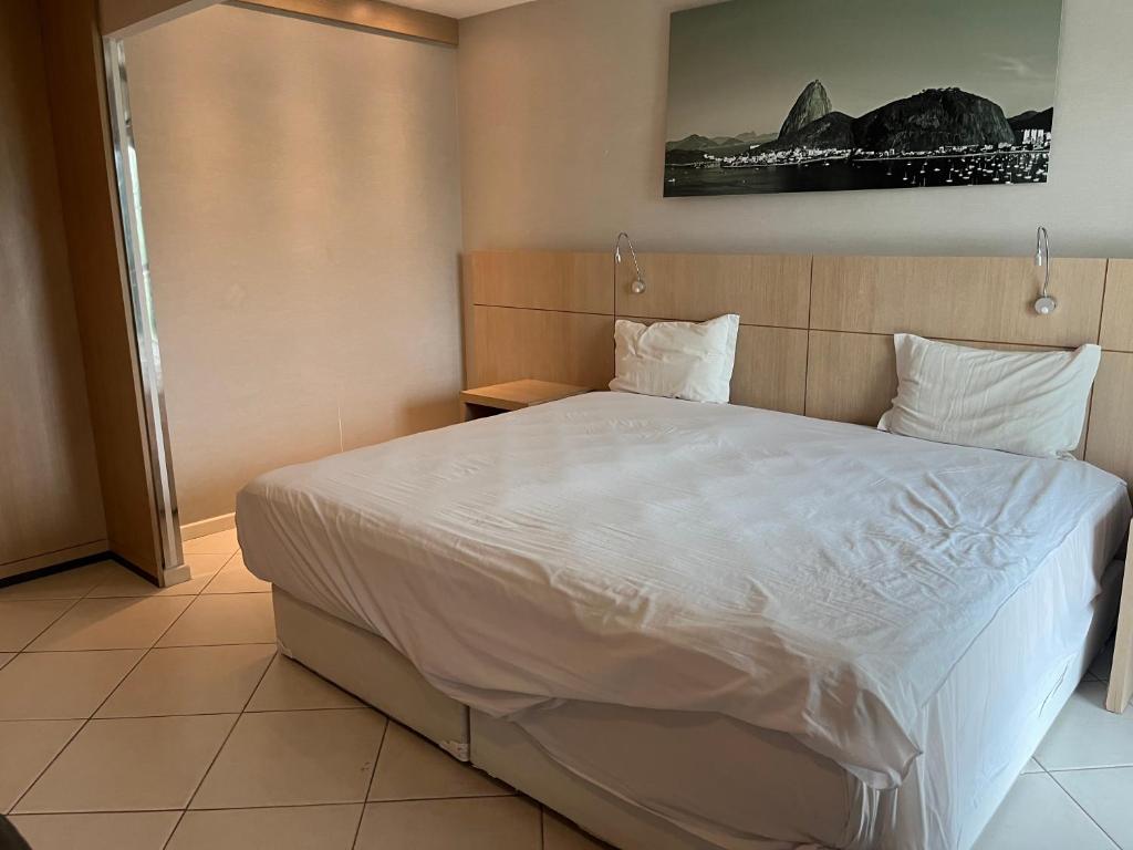 ein Schlafzimmer mit einem großen Bett mit weißer Bettwäsche und Kissen in der Unterkunft Hotel Quality Flat Barra da tijuca in Rio de Janeiro