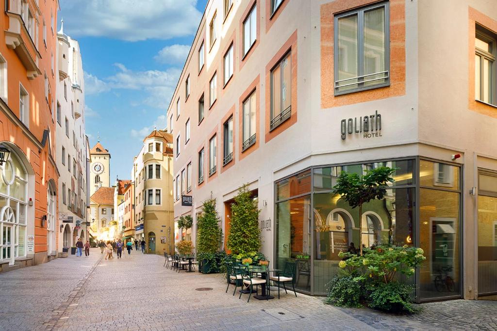 eine Stadtstraße mit Gebäuden und Tischen und einem Uhrturm in der Unterkunft Hotel Goliath am Dom in Regensburg