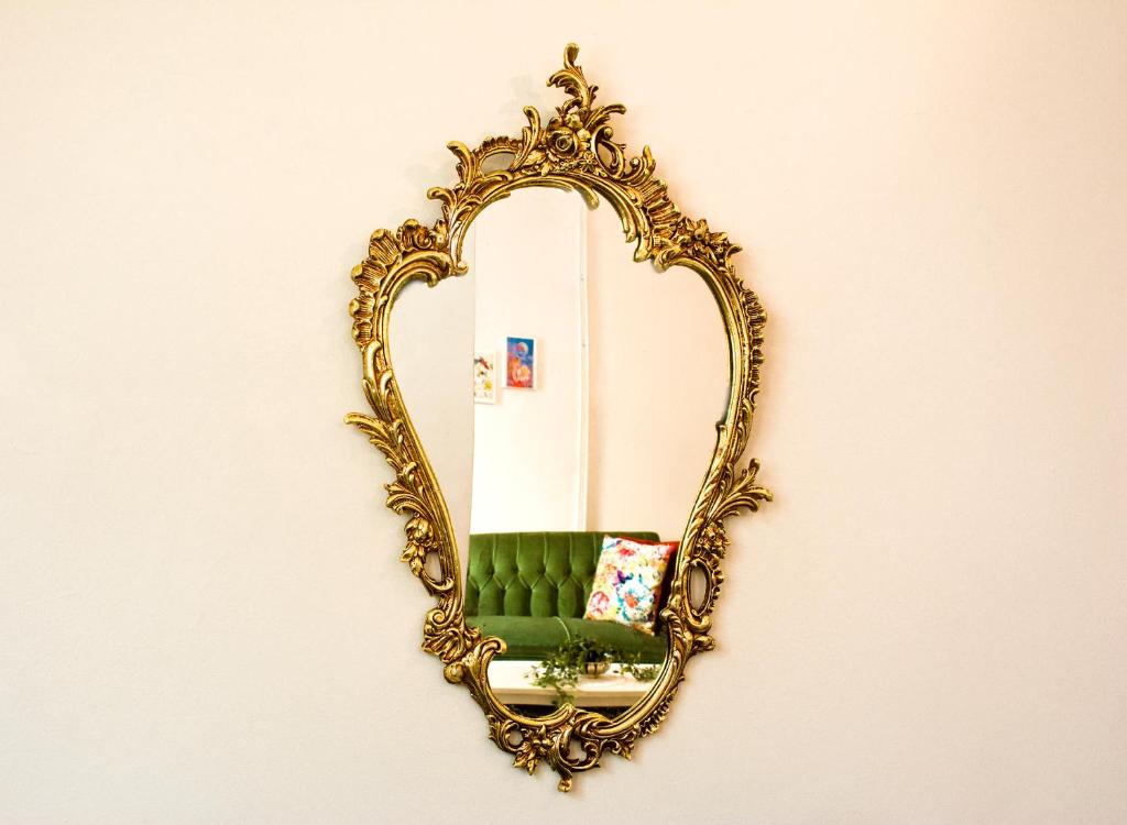 a gold mirror hanging on a wall with a green chair at Lilian's House in Chania