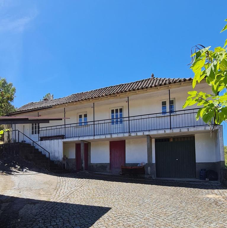 a white building with red doors and a balcony at Casa de Cabecinho- Albufeira do Azibo in Bragança